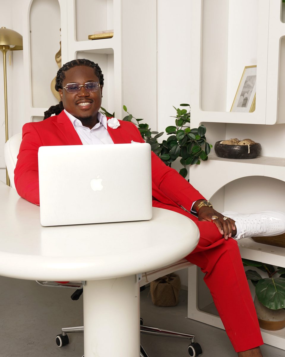 Edson Bienaime, owner and founder of Manivest, at his desk in a red suit